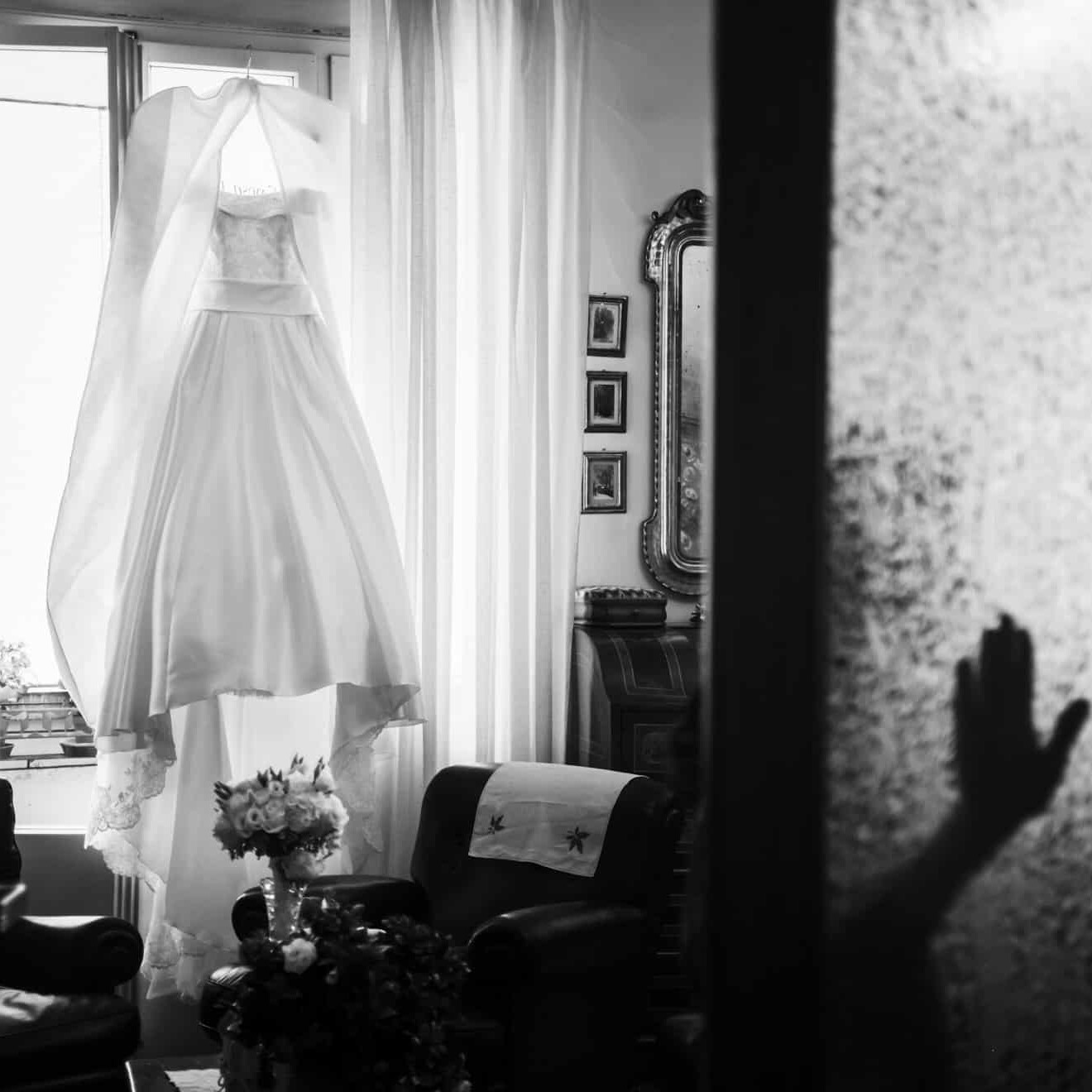 Una mano appoggiata sul vetro con l'abito della sposa di sfondo